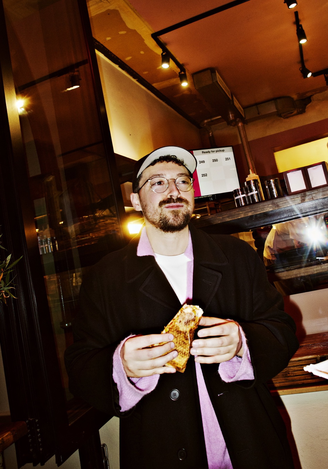 Daniel Wolfson nachts vor einem Imbiss mit Sandwich in den Händen